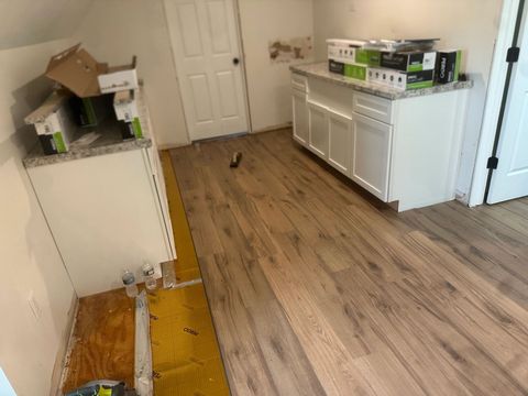 Luxury vinyl plank going down over yellow underlayment beside kitchen cabinets