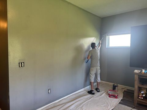 Painter rolling a gray wall with a pole roller, floor covered by a drop cloth