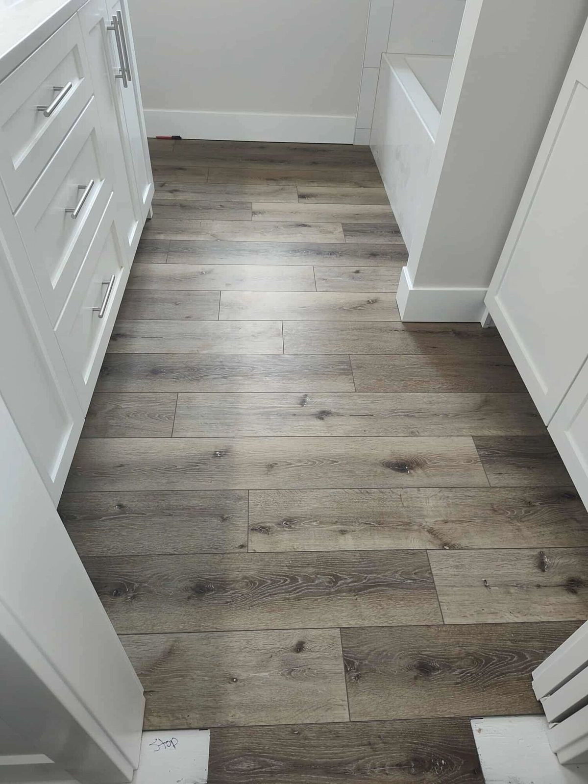 Finished gray wood-look vinyl plank floor in a hallway with white cabinets